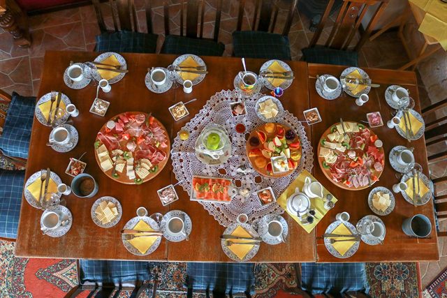 Reich gedeckte Frühstückstafel von oben: Platten mit Käse, Schinken, Lachs, frischem Obst und Konfitüren