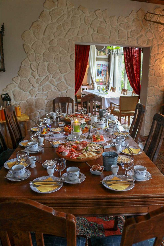 Lange, festlich gedeckte Tafel mit Frühstücksplatten, Eierbechern und gelben Servietten vor einer Natursteinwand
