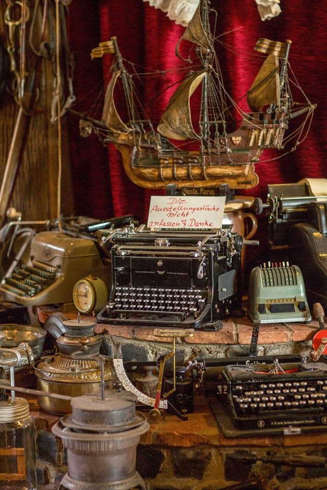Detail der Antiquitätensammlung: Modellsegelschiff „Santa Maria“ über alten Schreibmaschinen und Rechenmaschinen
